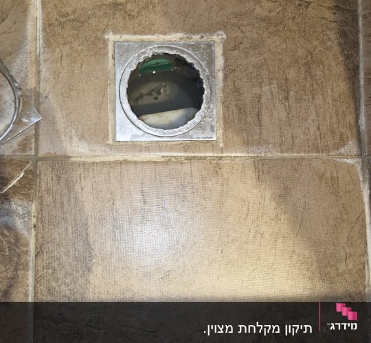 קופסת ניקוז רצפתית פתוחה ברצפת אריחים במהלך עבודת אינסטלציה